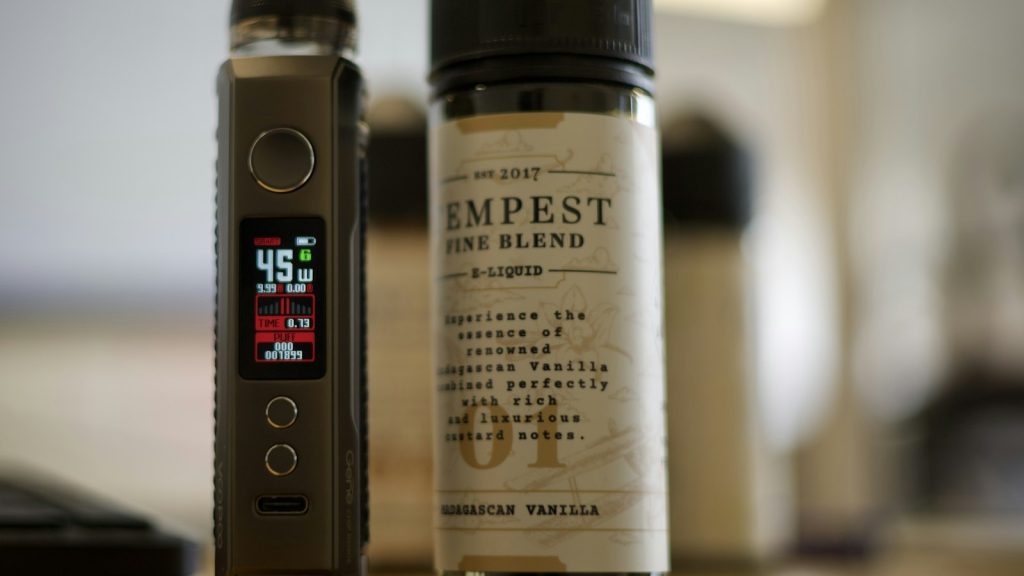 A pod-style vaping device beside a bottle of e-liquid